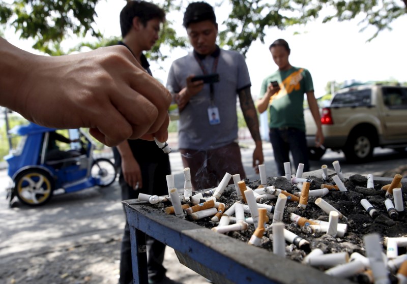 A smoker places a cigarette stub on a tray filled with stubs beside a road in Las Pinas